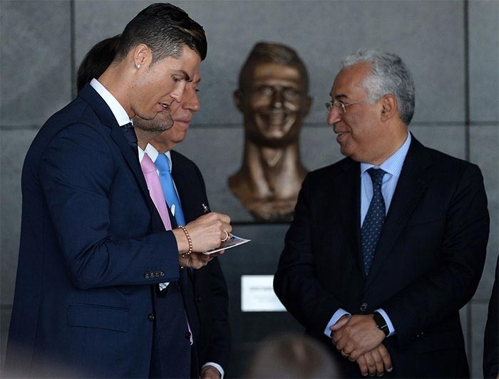 Portugaliya bosh vaziri Antonio Koshta Krishtianodan dastxat olmoqda, bu vaqtda orqadan sportchining yovuz haykali qarab turibdi
