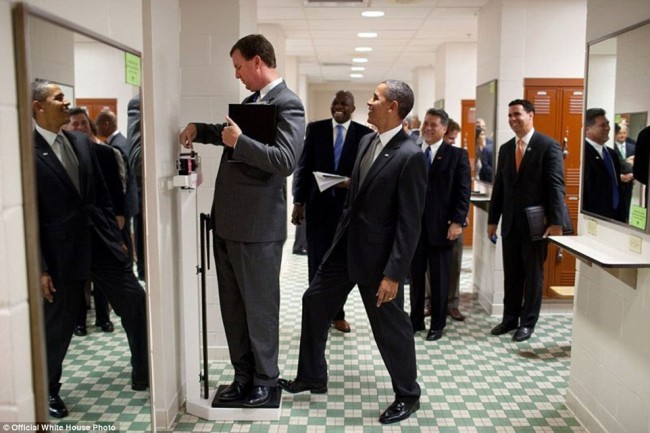 Prezident yordamchisi Marvin Nikolson Texas universitetining voleybol jamoasining kiyim almashtirish xonasida vaznini o’lchashga urinmoqda.
